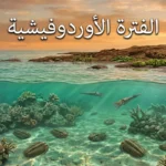 صورة توضيحية واقعية للفترة الأوردوفيشية تُظهر محيطاً قديماً ضحلاً يحتوي على شعاب مرجانية بدائية وكائنات بحرية مثل ثلاثية الفصوص ونوتيلويدات مع ساحل صخري تنمو عليه نباتات بدائية في مناخ دافئ ورطب