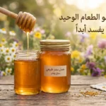 برطمان عسل طبيعي ذهبي مع ملعقة خشبية وأزهار برية – العسل هو الطعام الوحيد الذي لا يفسد أبداً